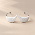 bewhile halo from the front on a sand background: a white under-eye band with a nose bridge and clear temple arms (mockup)